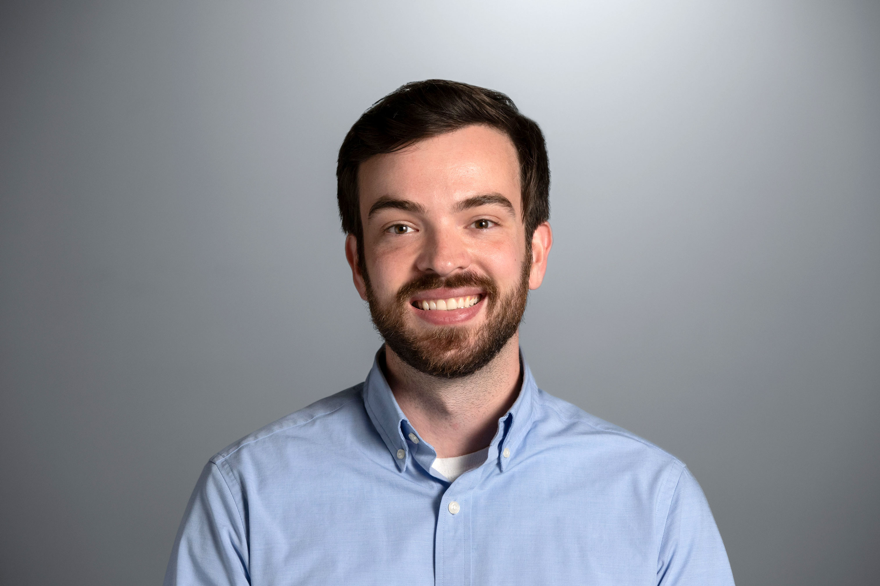 Jack is seen in front of a gray background wearing a light blue button down shirt 