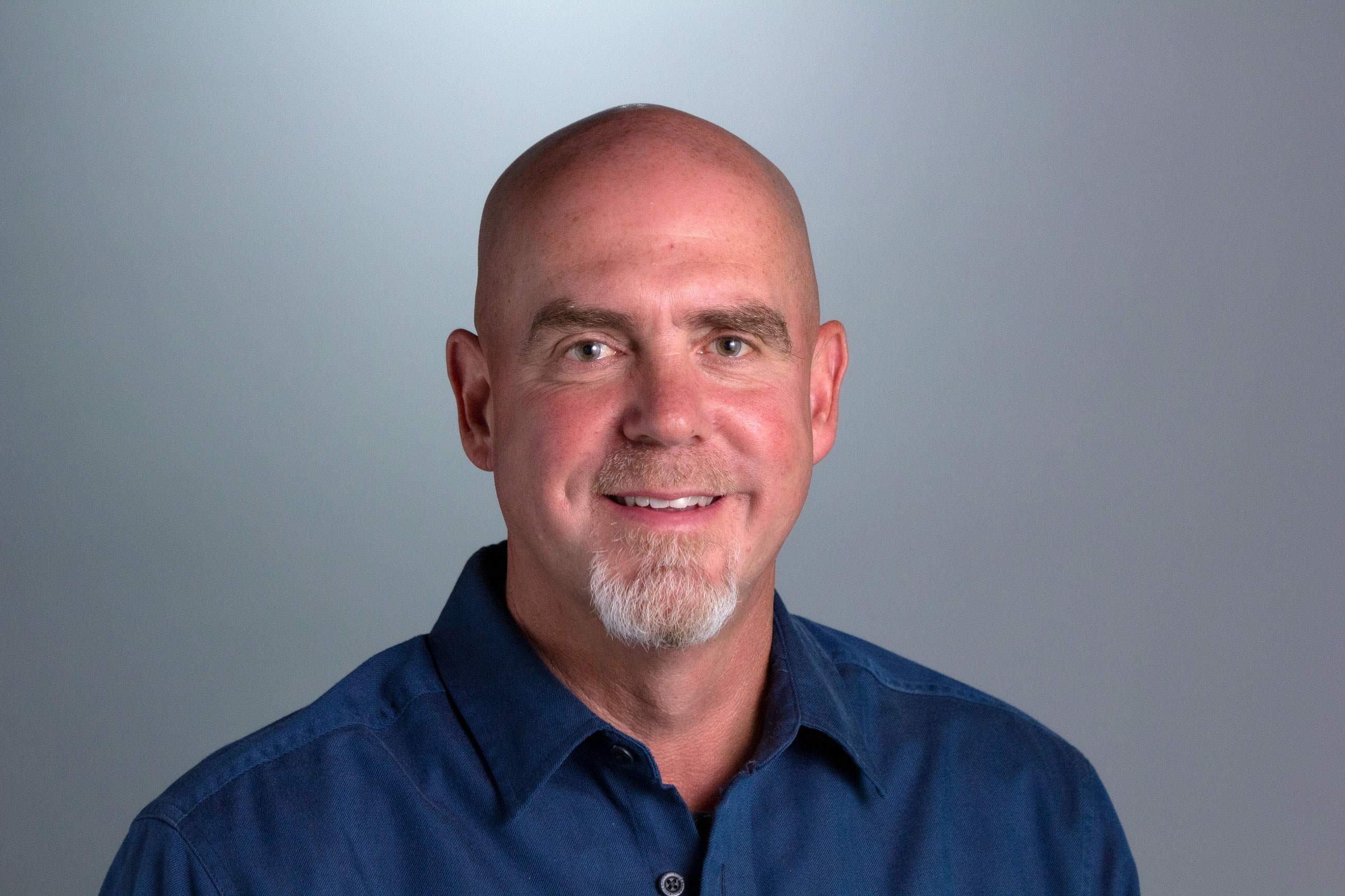 Headshot for Steve, who is seen in front of a gray backdrop wearing a navy blue button down shirt. 